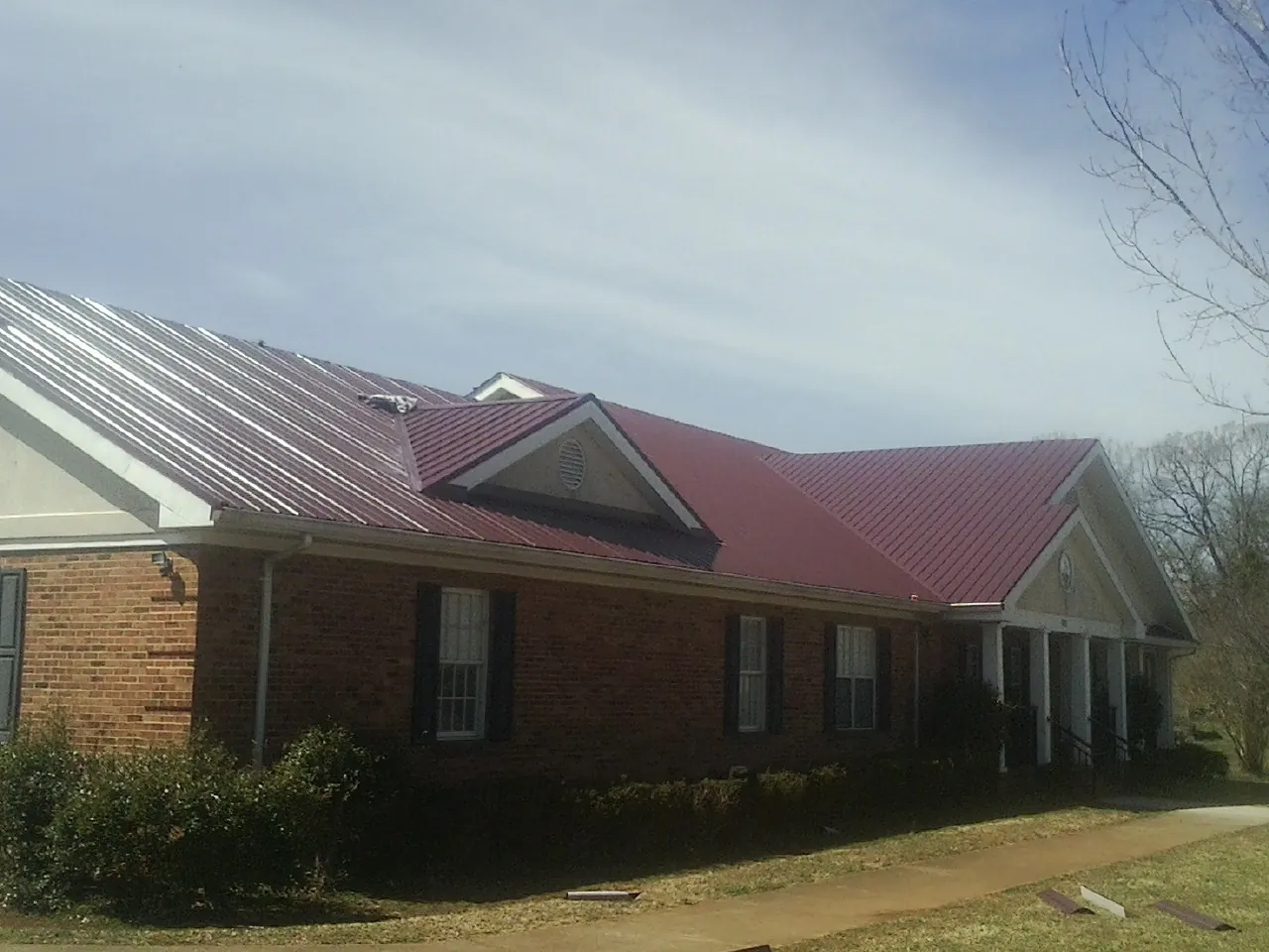 Red metal roof with gabled entries on a long brick building, from a Hail Damage Roof Repair job in Pilger