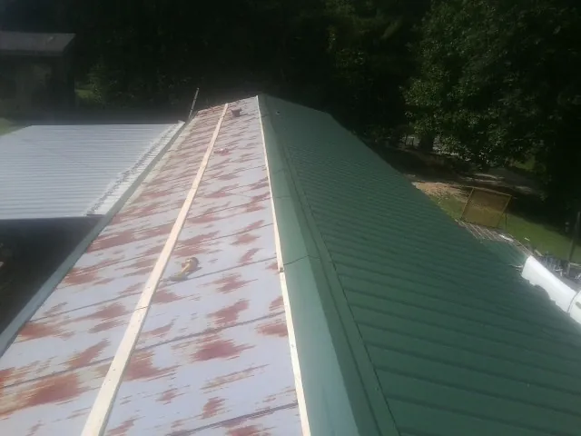 Old rusted panels beside newly installed green metal roofing — Wind Damage Roof Repair by Roofing Brothers in Pilger