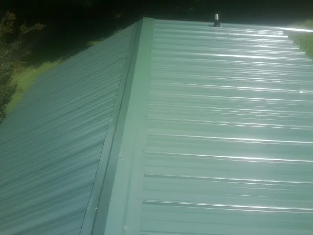 New green metal panels meeting at the ridge of a roof — Flat Roof Repair work by our crew in Pilger