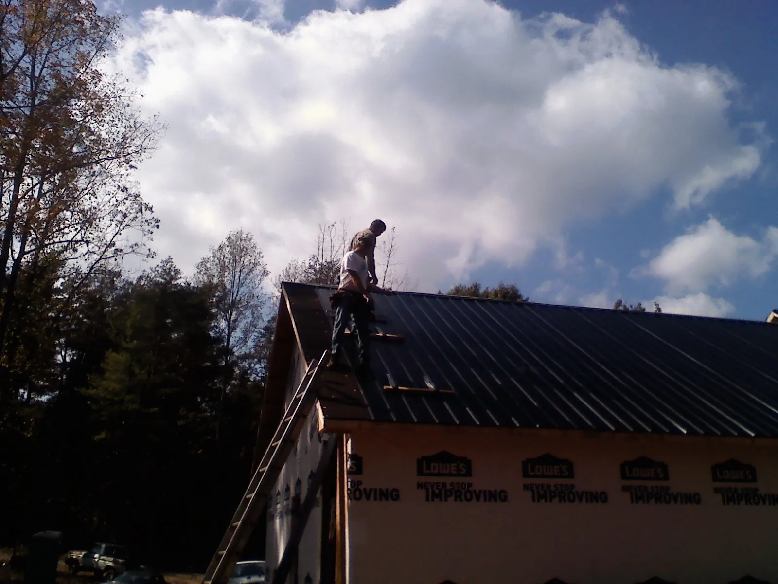 Roofer fastening dark metal panels high against a cloudy sky, from a Roof Inspection job in Pilger