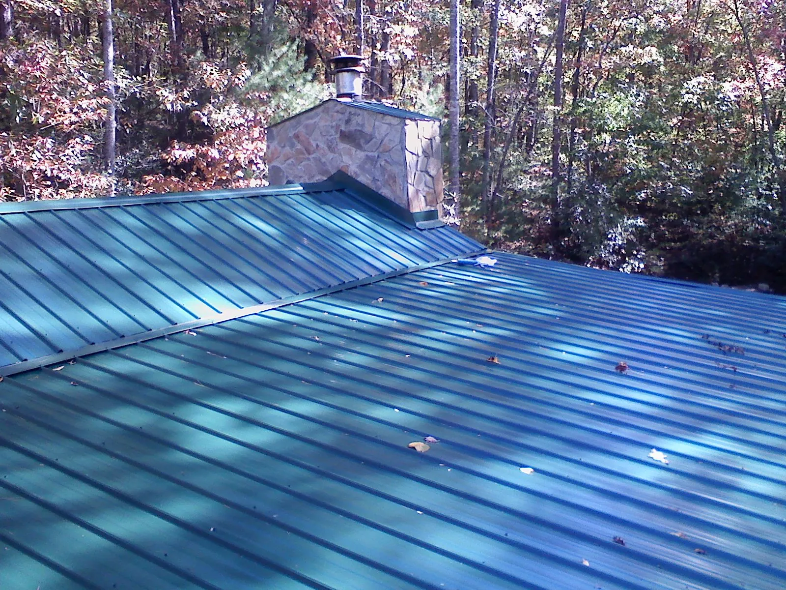New green metal roof and stone chimney surrounded by autumn woods in Pilger