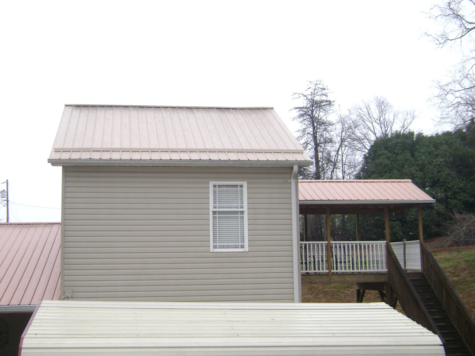 Tan metal roofs on a two story addition and attached porch, from a Roof Replacement job in Pilger
